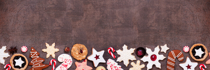 Christmas baking bottom border with an assortment of cookies and sweet treats. Top view on a dark stone banner background with copy space. Holiday baking concept. - obrazy, fototapety, plakaty