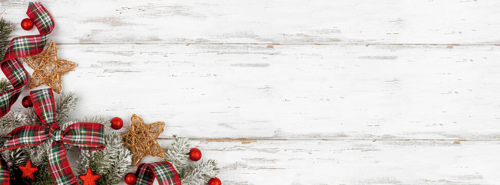 Christmas Corner Border Of Ornaments, Branches And Red And Green Plaid Bows And Ribbon. Top Down View On A White Wood Background. Copy Space.