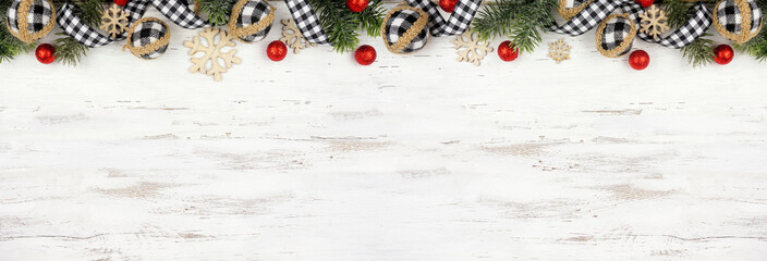 Christmas top border of white and black gingham ribbon, baubles and branches. Above view on a white wood banner background. Copy space.