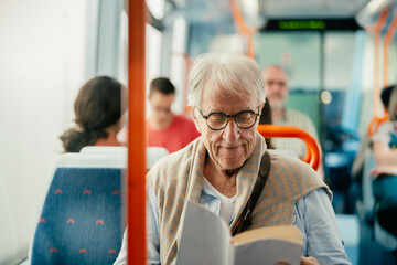 Senior man reading book while traveling with bus - 665783100