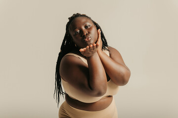Beautiful voluptuous African woman in underwear touching face and smiling on studio background