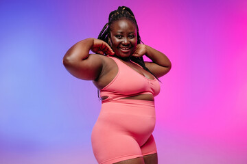 Obraz premium Voluptuous African woman in sportswear radiating self-love while standing on vibrant background