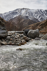 Stone bank of a mountain river with a fast current. Late autumn in the mountains