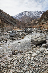 The bank of a small river flowing from the mountains. Autumn landscape in cloudy weather. Rocky creek shore