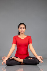 Fototapeta premium Healthy young woman in red t-shirt and black leggings doing yoga and stretching exercises isolated on grey background