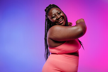 Voluptuous African woman in sportswear gesturing and smiling against vibrant background
