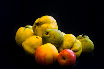 a still life with quinces and pears and apples and black background