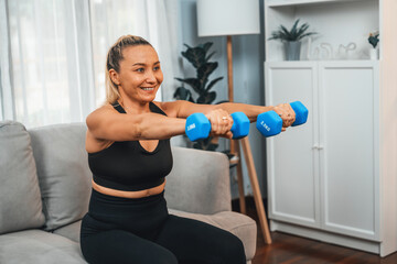 Fototapeta na wymiar Athletic and sporty senior woman engaging in body workout routine with lifting dumbbell at home as concept of healthy fit body with body weight lifestyle after retirement. Clout