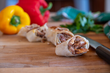 Shawarma pieces on wooden table with sweet peppers in the background and knife