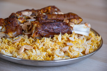 Plate of meat and rice topped with almonds on wooden table with top view