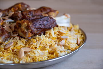 Plate of meat and rice topped with almonds on wooden table with top view