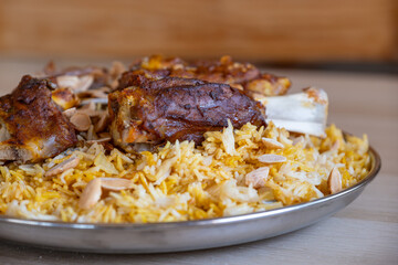 Plate of meat and rice topped with almonds on wooden table with top view