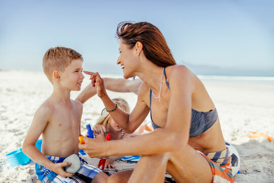 Happy young mother applying sunscreen to her son at the beach