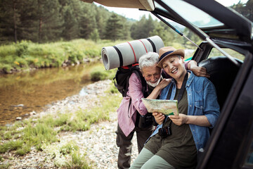 Elderly couple looking at a map on a trunk of a car in nature