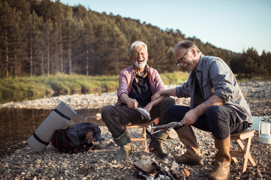 Two old friends cooking fish on a camping trip in the woods