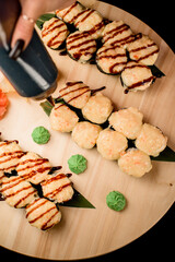 Set of sushi rolls with eel on a wooden board topped with unagi sauce from a black bottle. White and red ginger