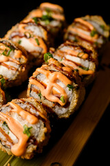 Baked sushi rolls with salmon, cheese, greens and sauce on a wooden board close up