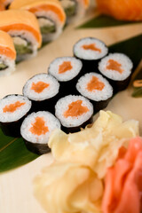 Assorted sushi rolls on a wooden board close up, red and white ginger