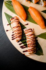 Assorted sushi rolls on a round wooden board on black table, salmon close up