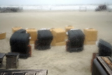 Blick bei Regenwetter durch die Fensterscheibe an der Seebrücke auf die Strandkörbe am Strand von St. Peter-Ording im Kreis Nordfriesland in Schleswig-Holstein im Herbst an der Küste der Nordsee