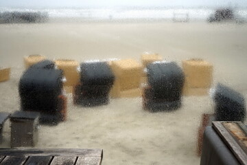 Blick bei Regenwetter durch die Fensterscheibe an der Seebrücke auf die Strandkörbe am Strand von St. Peter-Ording im Kreis Nordfriesland in Schleswig-Holstein im Herbst an der Küste der Nordsee