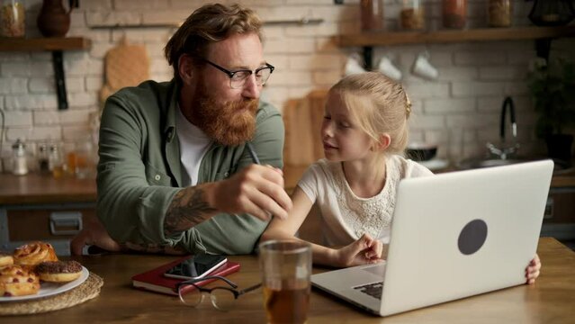 Child using laptop with tattooed father and talking near buns in kitchen at home