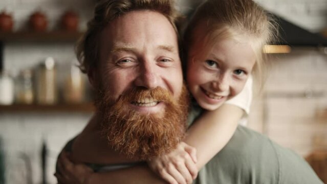 Portrait of cheerful girl hugging bearded father and looking at camera at home, slow motion