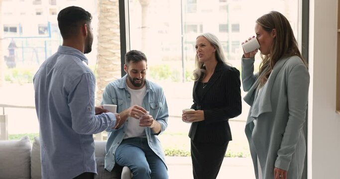 Group of young and mature multiethnic colleagues met in office hall blab enjoy warm conversation during coffee break. Friendly teammates having informal talk, drink tea, chatting, distracted from work