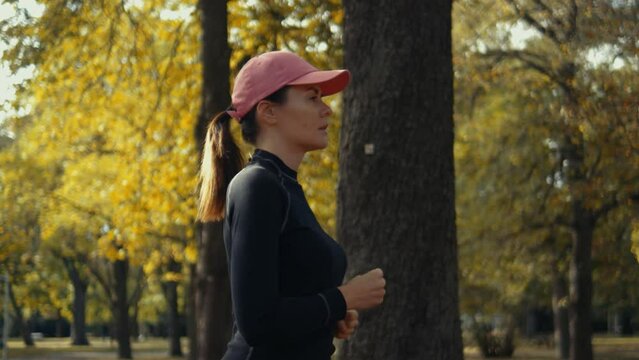 A young woman runner training in aautumn park. Close up of fitness girl is jogging outdoor. Running and healthy lifestyle. Slow motion