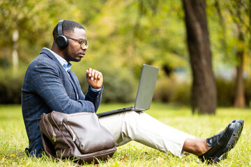 Young businessman with headphones and laptop computer working in park outside the office.