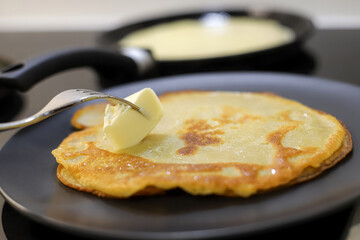 Making bliny at home. Closeup of traditional thin pancakes being buttered with silver fork. Photo with selective focus
