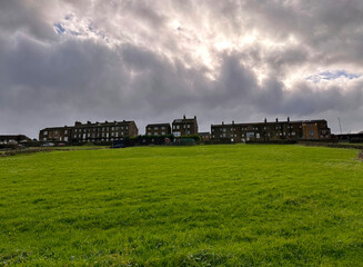 Fototapeta na wymiar Heavy thunder clouds, with Victorian houses on the horizon, overlooking extensive grassland near, Low Lane, Queensbury, UK