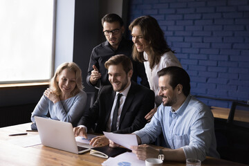 Smiling group of different ages businesspeople do corporate research together use laptop, talking via video call. Business team brainstorming on meeting in office. Technology, collaboration, teamwork