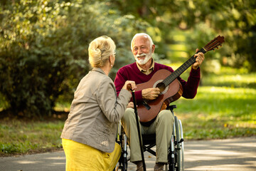Elderly man in wheelchair playing guitar and enjoying the moment with his wife.