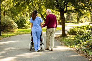 Obraz premium Nursing assistant and senior people walking together in the park.