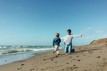 A young mother and her three-year-old son run, play, smile, and laugh on the seashore.