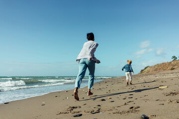 A young mother and her three-year-old son run, play, smile, and laugh on the seashore.