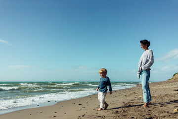 A young mother and her three-year-old son run, play, smile, and laugh on the seashore.