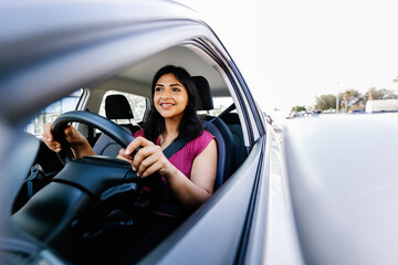 Happy young indian woman driving new car in the city. Rental car service concept