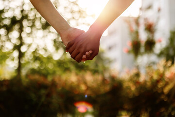 Two unrecognizable young diverse women holding hands over city background. Close up rear view of lesbian couple standing together outdoors. Sunlight. Copy space - Powered by Adobe