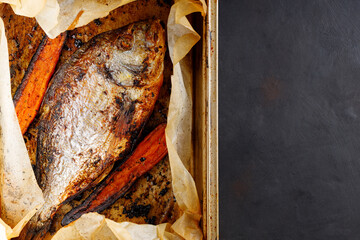 Baked dorado fish with golden crust and carrot on baking tray. Top view. Copy space