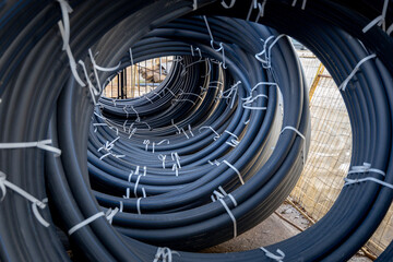 Coils of black polyethylene pipes for laying high voltage electrical cables underground at a construction site. Electrical insulation - obrazy, fototapety, plakaty