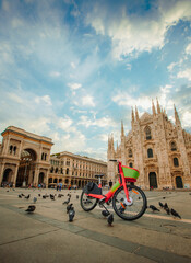 Close up on public electric bike in Piazza Duomo in Milan with Milan Cathedral and Galleria Vittorio Emanuele, vertical view