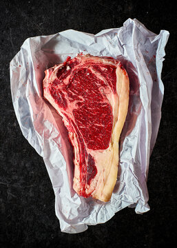 Basque Txuleton Steak or Prime Bone-in ribeye steak wrapped in butcher paper, placed on a black marble background.