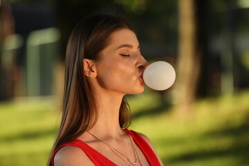 Beautiful young woman blowing bubble gum in park