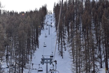 Chair lifts in Italian ski resort Sauze D'Oulx. Overhead chair lift for skiers and snowboarders moving through a thick snowy woodland on a sunny winter's day.