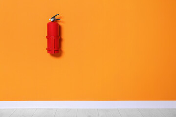 Red fire extinguisher on orange wall. Space for text