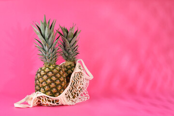 Whole ripe pineapples and net bag on pink background, space for text