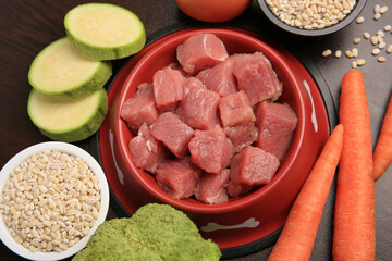 Raw meat in bowl and healthy products for pet on black background, flat lay