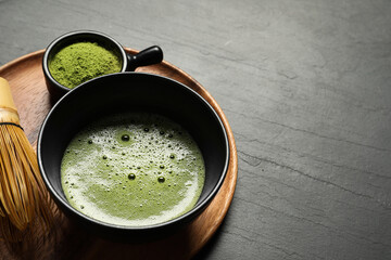 Cup of fresh matcha tea, bamboo whisk and green powder on black table, space for text